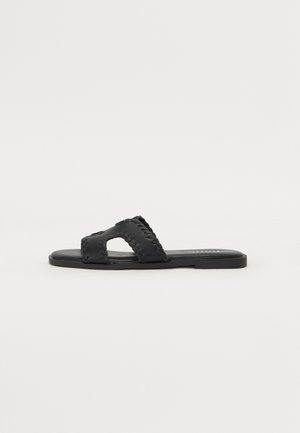 Zwarte platte sandalen met een brede dubbele band en uitgesneden ontwerp, met gestikte details langs de randen en een gladde zool.