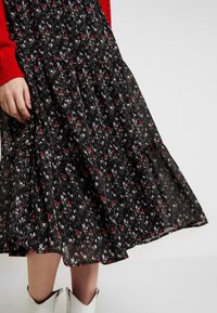 Svart blommig midi kjol med små röda och vita blommor, bärs med vita ankelstövlar och en röd stickad tröja där ärmen är synlig.