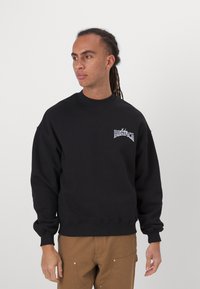 Black sweatshirt with a round neckline and ribbed cuffs. Features a small graphic on the chest. Soft, textured material.