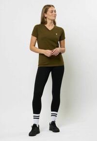 Olijfgroene T-shirt met korte mouwen en V-hals, aansluitende pasvorm, gecombineerd met zwarte leggings en zwarte sneakers, met witte gestreepte sokken.