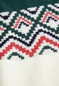 Sweter dziergany z geometrycznym wzorem w kolorach zielonym, granatowym i czerwonym na kremowym tle. Miękka tekstura z różnorodnymi detalami ściegów.