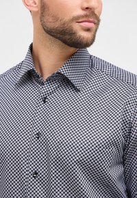 Zwart-wit gestreept shirt met een geometrisch ontwerp, knoopsluiting aan de voorkant en een puntige kraag. Zachte stof met een gladde textuur.