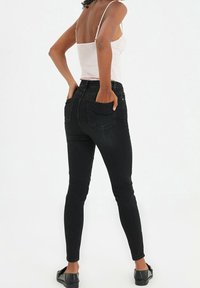 Black skinny jeans made of denim, featuring a high waist, back pockets, and a smooth texture, paired with a light pink top.