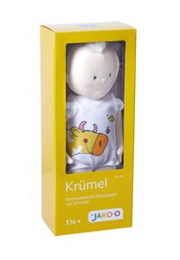 Soft-bodied doll with a smiling face, wearing a white onesie featuring a cow design, presented in a bright yellow box with clear front.