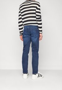 Suéter a rayas en blanco y negro, jeans de mezclilla azules y zapatillas blancas con acentos negros. Enfoque en la vista trasera del conjunto.