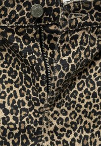 Veste en denim avec imprimé léopard, présentant un motif noir et beige, fermeture à pression métallique et devant zippé. Tissu texturé avec des détails contrastés.