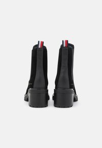 Černé kotníkové boty s nubukovým povrchem, blokovým podpatkem a kontrastními červenými a námořnickými poutky. Disponují minimalistickým designem a robustní podrážkou.