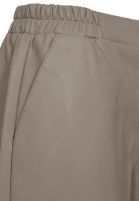 Close-up van beige leren broeken met een elastische tailleband en een zijzak met zichtbare stikdetails.