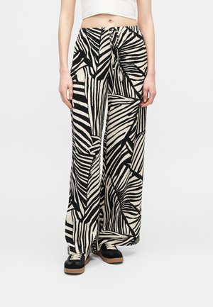 Persoon die wijde broek met zwart-witte abstracte zebra-strepen draagt, gecombineerd met zwarte schoenen en een cropped wit topje.