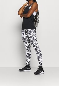 Musta urheilu-toppi, joka on kerroksittain valkoisen urheiluliivin päällä, yhdistettynä mustiin ja valkoisiin abstraktikuosisin leggingsin ja mustiin juoksukenkiin.