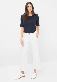 Top corto blu navy abbinato a pantaloni bianchi a gamba larga con un delicato motivo a righe, completato da sneakers bianche con suola color sabbia.