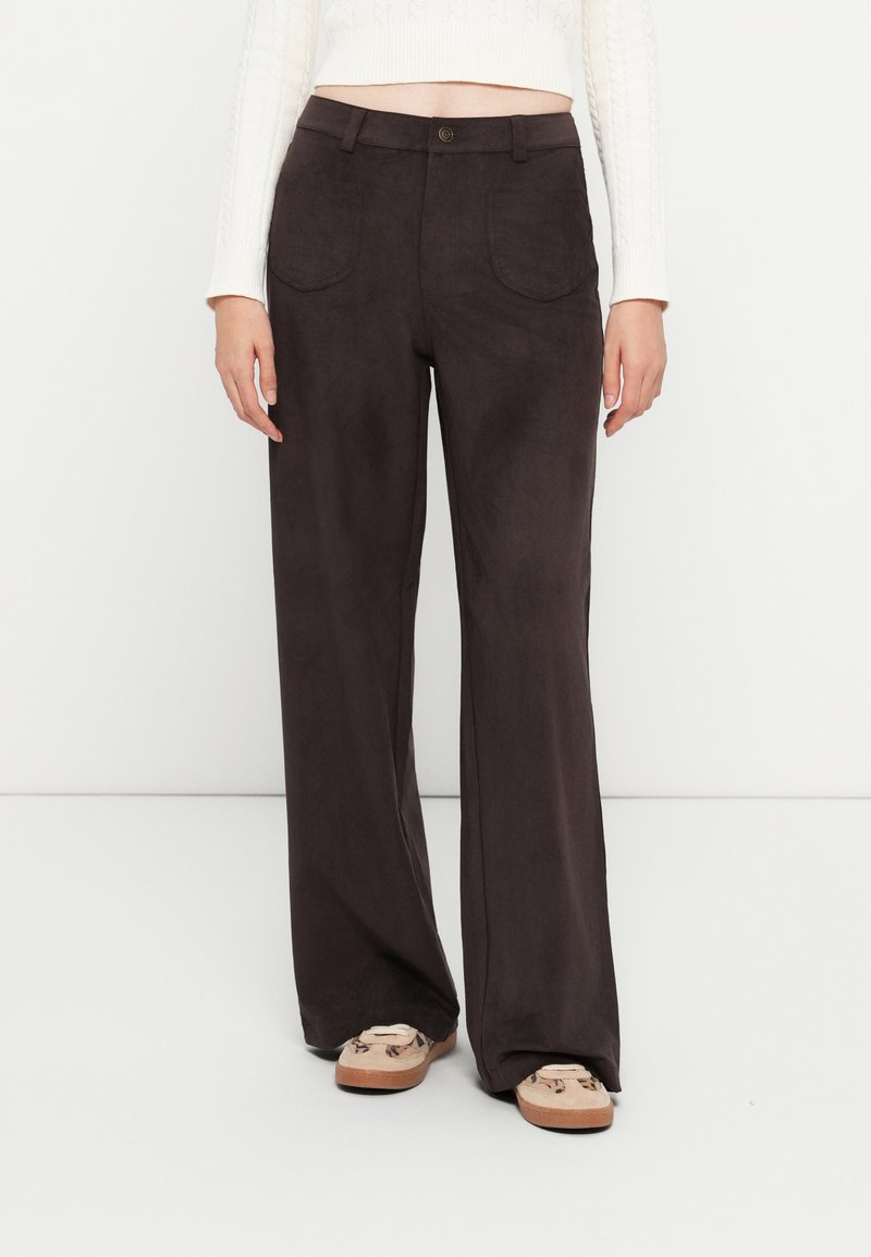 Pantalones de pierna ancha de color marrón oscuro, confeccionados con una suave tela parecida al ante. Cuentan con dos bolsillos frontales y un cierre con un solo botón.
