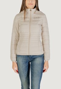 Giacca leggera beige trapuntata con colletto alto, zip frontale e logo sul petto. Maniche lunghe con polsini elastici, due tasche laterali.