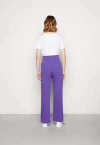 Lila vida byxor i mjukt tyg med hög midja. Kombinerat med en enkel vit skjorta med kort ärm och vita sneakers.