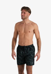 Zwemshorts met een donkergroen tropisch bladenpatroon, lichtgewicht stof, elastische tailleband met trekkoord, en een klein logo detail op het been.