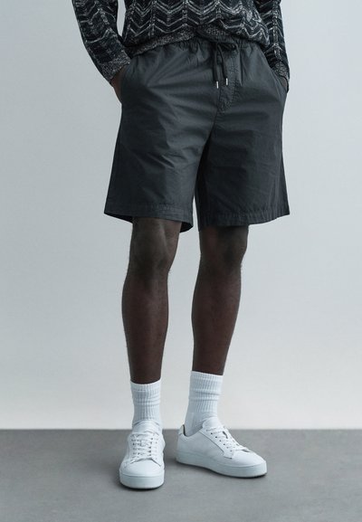 Shorts légers noirs avec une taille élastique et un cordon de serrage, associés à des baskets blanches et des chaussettes montantes.