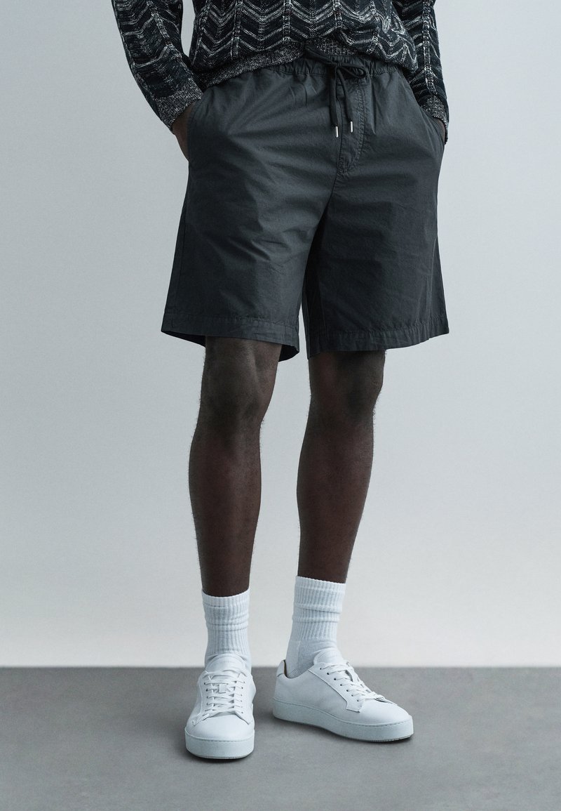 Czarne lekkie szorty z elastycznym pasem i sznurkiem, w połączeniu z białymi tenisówkami i skarpetkami do połowy łydki.