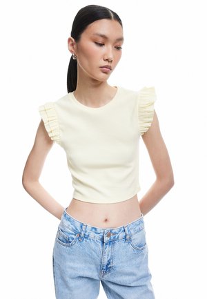 Gul ribbet crop top med flæseærmer. Båret med høj talje lyseblå jeans. Glat tekstur, tætsiddende design og rund halsudskæring.