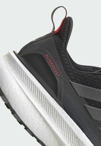 Black athletic shoe with a textured upper, featuring a red accent and "ULTRAGBOOST" text. White, curved midsole with a patterned finish.