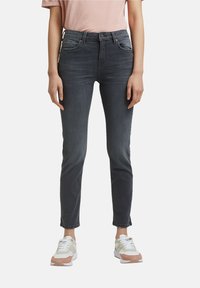 Mujer vestida con jeans ajustados de cintura alta en gris oscuro con dobladillos deshilachados y zapatillas blancas con acentos en beige y marrón.