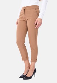 Pantaloni marroni slim-fit con una texture liscia, dotati di chiusura a bottone, tasche laterali e orli arrotolati, abbinati a tacchi neri a punta.