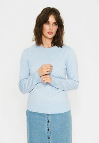 Svetlo modra pletena pulover s okroglim izrezom, dolgimi rokavi in diskretnimi naborki na ramenih, v kombinaciji z jeans krilom z detajli gumbov.