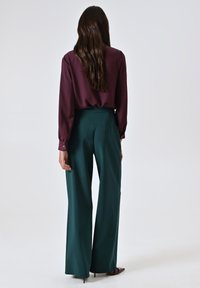 Blusa bordeaux a maniche lunghe abbinata a pantaloni teal a vita alta e a gamba larga. Tessuto morbido con una leggera lucentezza, design semplice e vestibilità sartoriale.