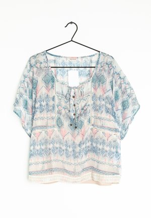 Let, løs bluse med pastelfarvede geometriske og blomsteragtige mønstre, korte ærmer, bindebånd og knapdetaljer ved halsudskæringen, hængende på en sort bøjle.