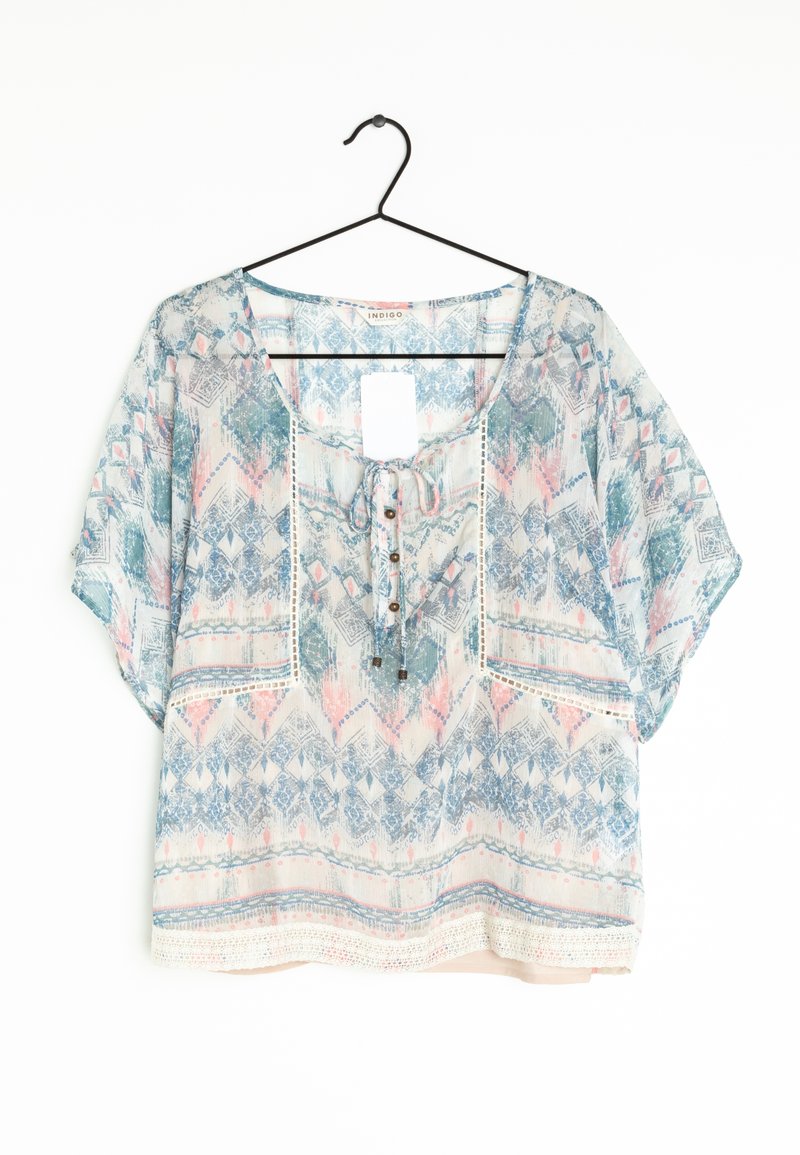 Blouse légère et ample avec des motifs géométriques et floraux pastel, manches courtes, détails de lien et boutons au niveau de l'encolure, suspendue sur un cintre noir.