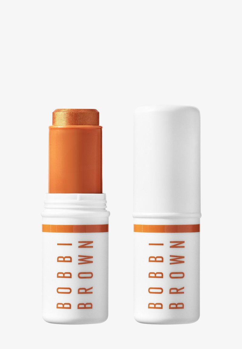 Stick bronzant scintillant Bobbi Brown dans un emballage orange, le capuchon retiré et placé à côté sur un fond blanc.