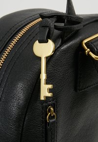 Schwarze Ledertasche mit einem goldenen Schlüssel-förmigen Reißverschlussanhänger, passendem goldenen Beschlägen und strukturierten Oberflächen. Der Reißverschluss verläuft entlang der oberen Kante.