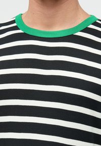 Svart-hvitt stripet T-skjorte med en grønn ribbestrikket rund hals. Stoffet ser mykt ut med en jevn tekstur og ensartet mønstring.