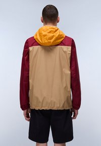 Vindjakke i maroon, gul og beige. Letvægts, med hætte og elastisk kant. Glat overflade, minimalistisk design.