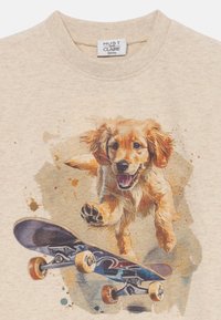 Beige T-Shirt mit einer bunten Illustration eines laufenden Golden Retrievers auf einem Skateboard, umgeben von Farbspritzern im Hintergrund.