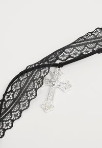 Schwarzes Spitzen-Choker mit einem silbernen dekorativen Kreuzanhänger, geschmückt mit klaren Edelsteinen, der eine nostalgische Ästhetik hervorruft.