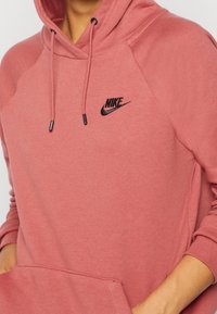 Hoodie i bomullsblandning i dämpad rosafärg med pungficka, ribbade muddar, dragsko i huvan och svart Nike-logotyp på bröstet.