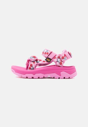Pink outdoor sandal with thick sole, adjustable straps featuring a cherry pattern, and a Teva brand logo on the side strap.