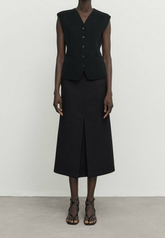 Gilet noir sans manches avec un décolleté en V profond et des boutons sur le devant, associé à une longue jupe noire avec une fente à l'avant et un design minimaliste.