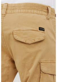 Kaki cargo kratke hlače s elastičnim pojasom, stražnjim džepom s preklopom i šivenim detaljima. Imaju malu crnu oznaku s natpisom "NINETEEN NINETY THREE."