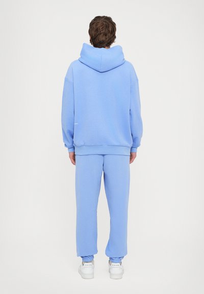 Lyseblå hættetrøje og matchende sweatpants lavet af blødt stof. Hættetrøjen har en stor hætte og ribbede manchetter. Sneakers fuldender outfittet.