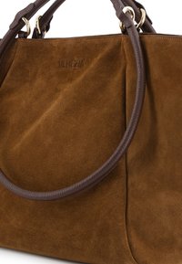 Braune Wildleder-Handtasche mit dunkelbraunen Ledergriffen. Sie besitzt ein dezent geprägtes Logo und eine glatte, weiche Textur im gesamten Design.