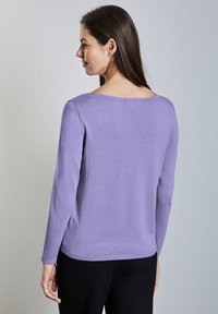 Suéter de manga larga en lavanda, confeccionado en una tela suave, con un escote amplio y dobladillo acanalado. La parte posterior tiene un acabado liso sin patrones visibles.