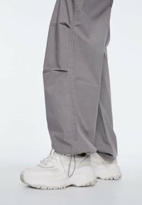 Szare spodnie cargo z bocznymi kieszeniami i luźnym krojem, zestawione z masywnymi białymi tenisówkami. Tekstura wydaje się gładka, z delikatnymi detalami szwów.