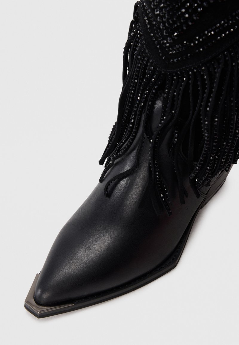 Stivale alla caviglia in pelle nera con punta affusolata, decorato con frange nere e dettagli in perline, e un coprisuola metallico testurizzato.