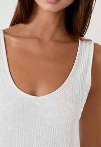 Canotta a coste grigio chiaro con scollatura a barca e spalline larghe. Il tessuto appare morbido con una leggera texture e un motivo sobrio.