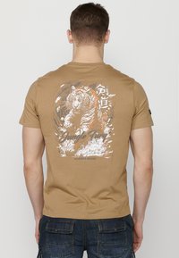 T-shirt à manches courtes beige avec un graphisme de tigre, des accents blancs et oranges, le texte "Jungle Fun" et une coupe décontractée.