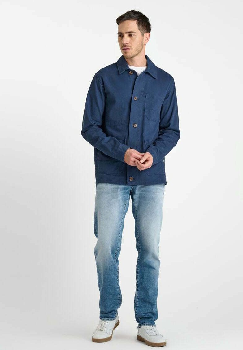 Navyblauwe katoenen jack met knopenfront, puntkraag en borstzak, gecombineerd met lichte denim jeans en witte sneakers.