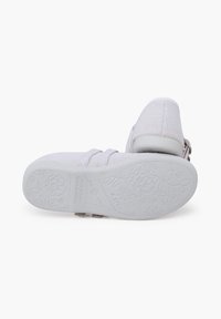 Chaussure en tissu texturé blanc avec un design de sangle et un motif floral en relief sur une semelle en caoutchouc blanc uniforme.