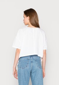 T-shirt branca curta com mangas curtas, decote reto e fecho nas costas. Combinado com jeans de cintura alta em azul claro com bolsos traseiros.