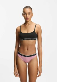 Zwarte bralette met dunne bandjes en een brede zwarte band met het label "HUGO"; gecombineerd met roze slip met een vergelijkbare zwarte band, gladde textuur.